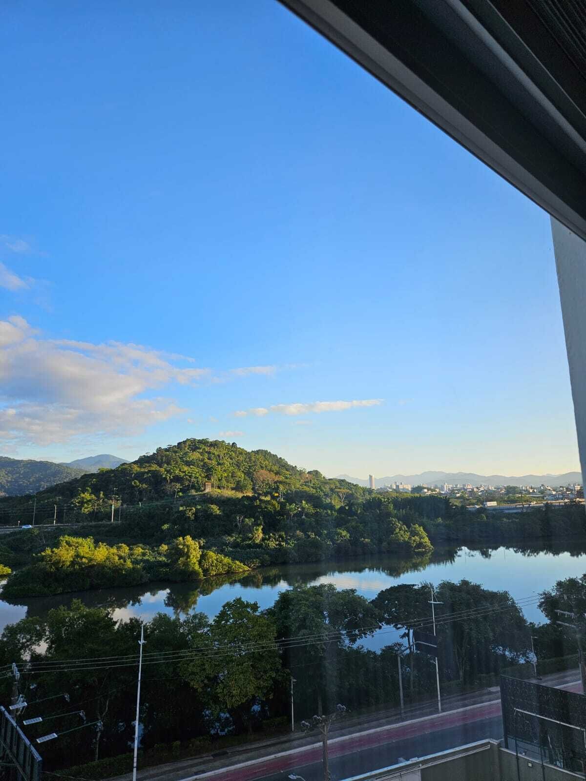 A view of a lake surrounded by hills, with a road in the foreground and a clear sky.