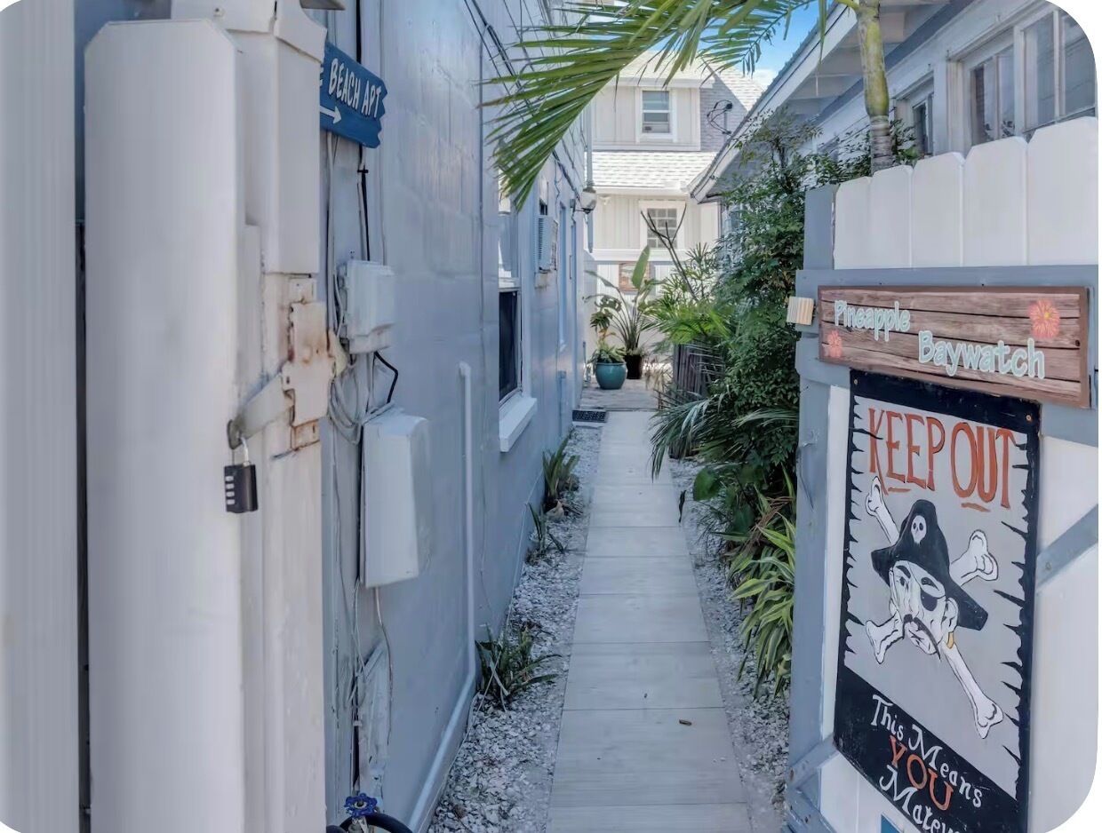 A narrow pathway flanked by buildings, a sign indicating 'Beach Front', and a 'Keep Out' sign with a ghost illustration.