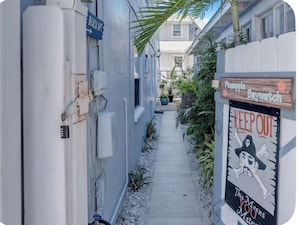 En smal gångväg som löper längs med byggnaderna, en skylt som visar vägen till stranden och en skylt med texten ”Håll dig borta” och en illustration av ett spöke.