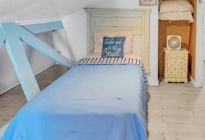Ein Schlafzimmer mit einem Bett, einem Kissen mit Aufschrift, einem Nachttisch mit Ventilator und einer kleinen Kommode.
