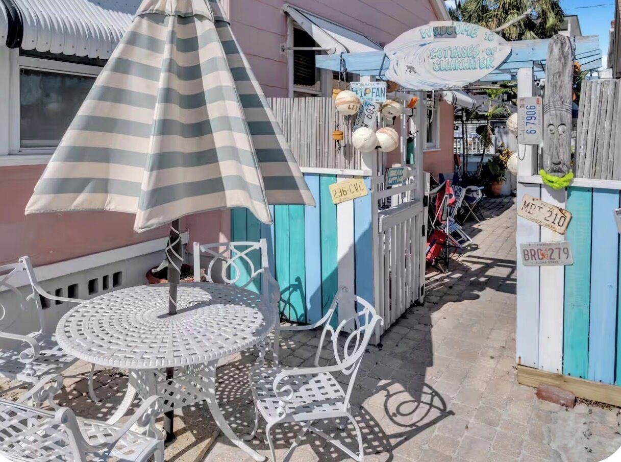 Un espace patio agrémenté d’un parasol à rayures, d’une table ronde en métal et de chaises en métal blanches.