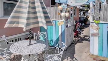 Un espace patio agrémenté d’un parasol à rayures, d’une table ronde en métal et de chaises en métal blanches.