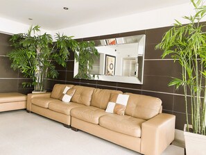 Un salon moderne avec un canapé en cuir beige, un grand miroir et des plantes vertes.