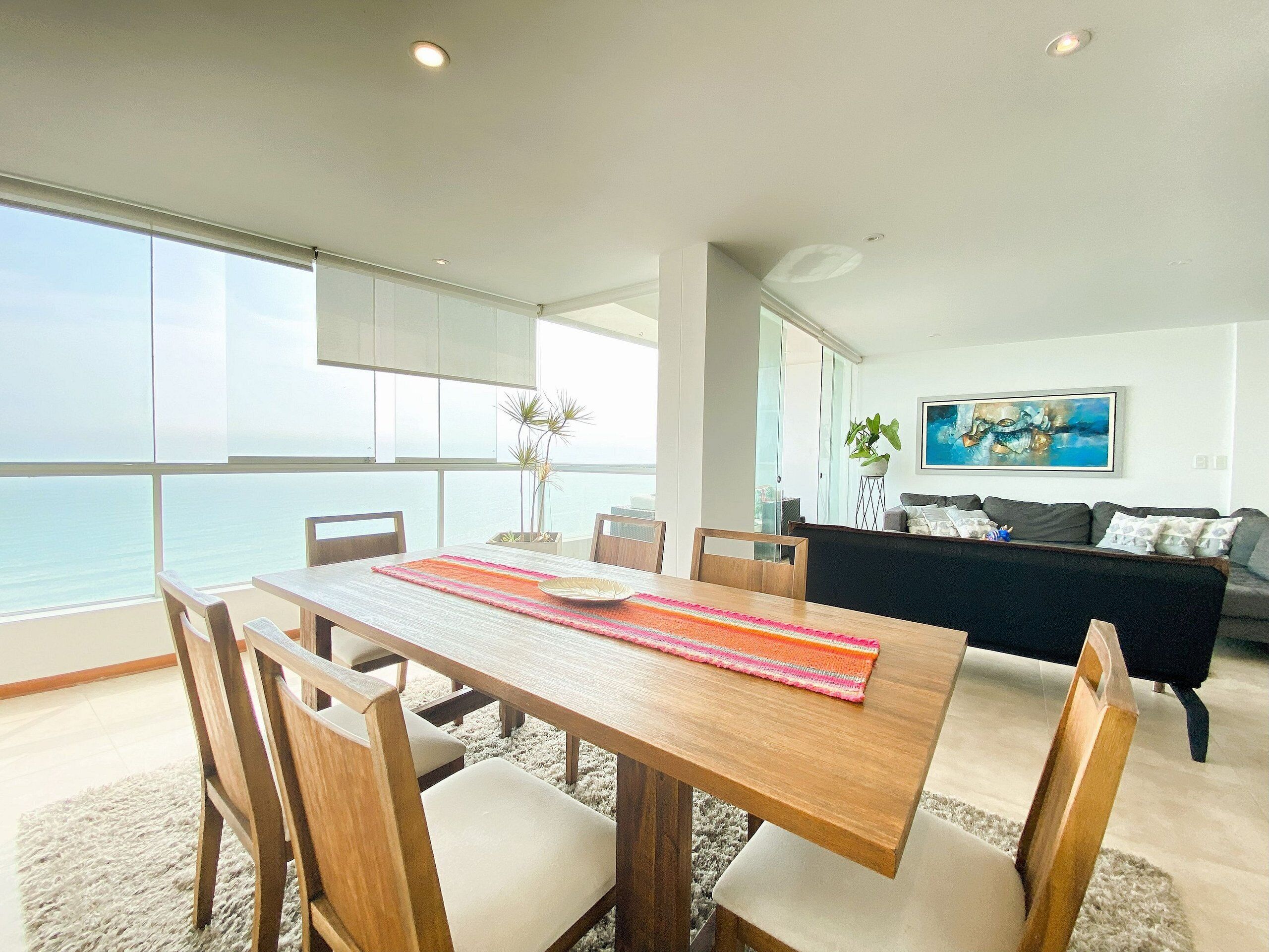 A modern living space with a dining area, a sofa, and a view of the sea.