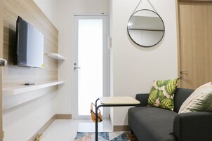 A living room with a flat-screen TV mounted on the wall, a round mirror, a sofa with patterned cushions, and a small table.