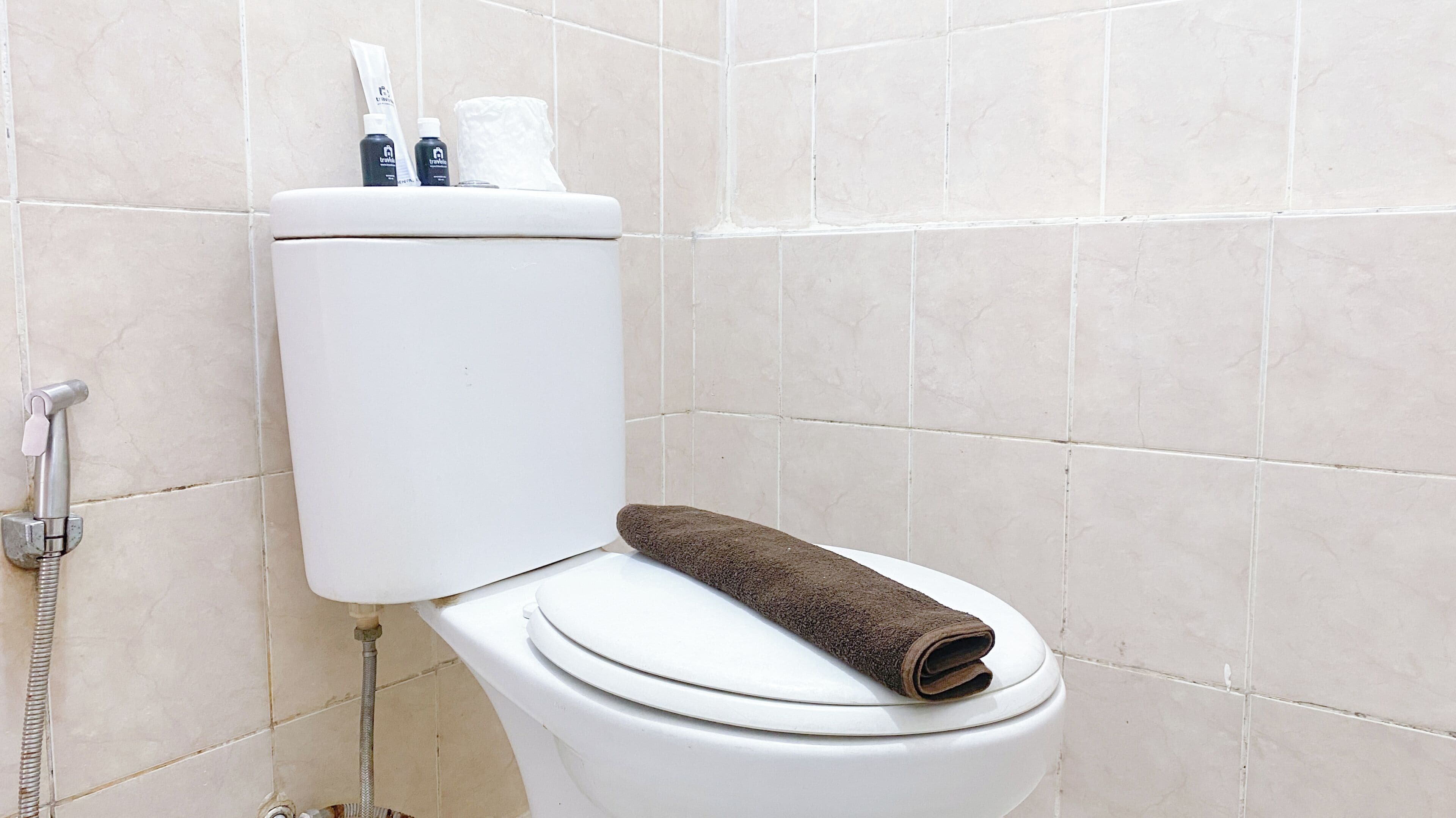 A toilet with a towel on the seat, a toilet paper roll, and a bottle of hand soap.