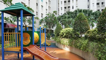 Ein Spielplatz mit Rutsche und Klettergerüsten, umgeben von Grünflächen und einem Gebäude im Hintergrund.