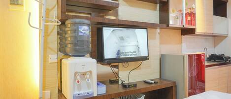 Espaço compacto com dispensador de água, televisão e uma pequena cozinha.