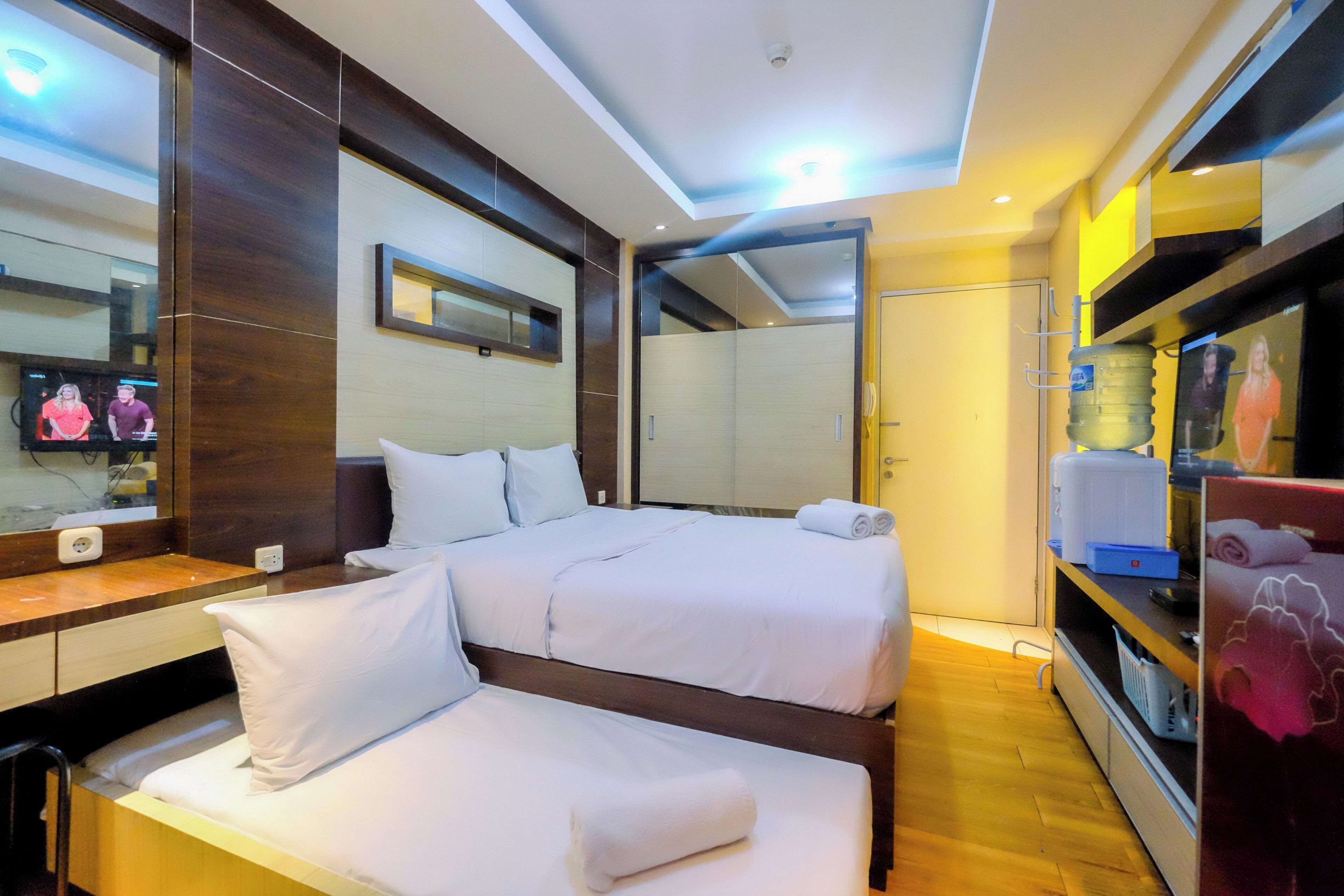 A hotel room with two beds, a large mirror, a television, and a water dispenser.