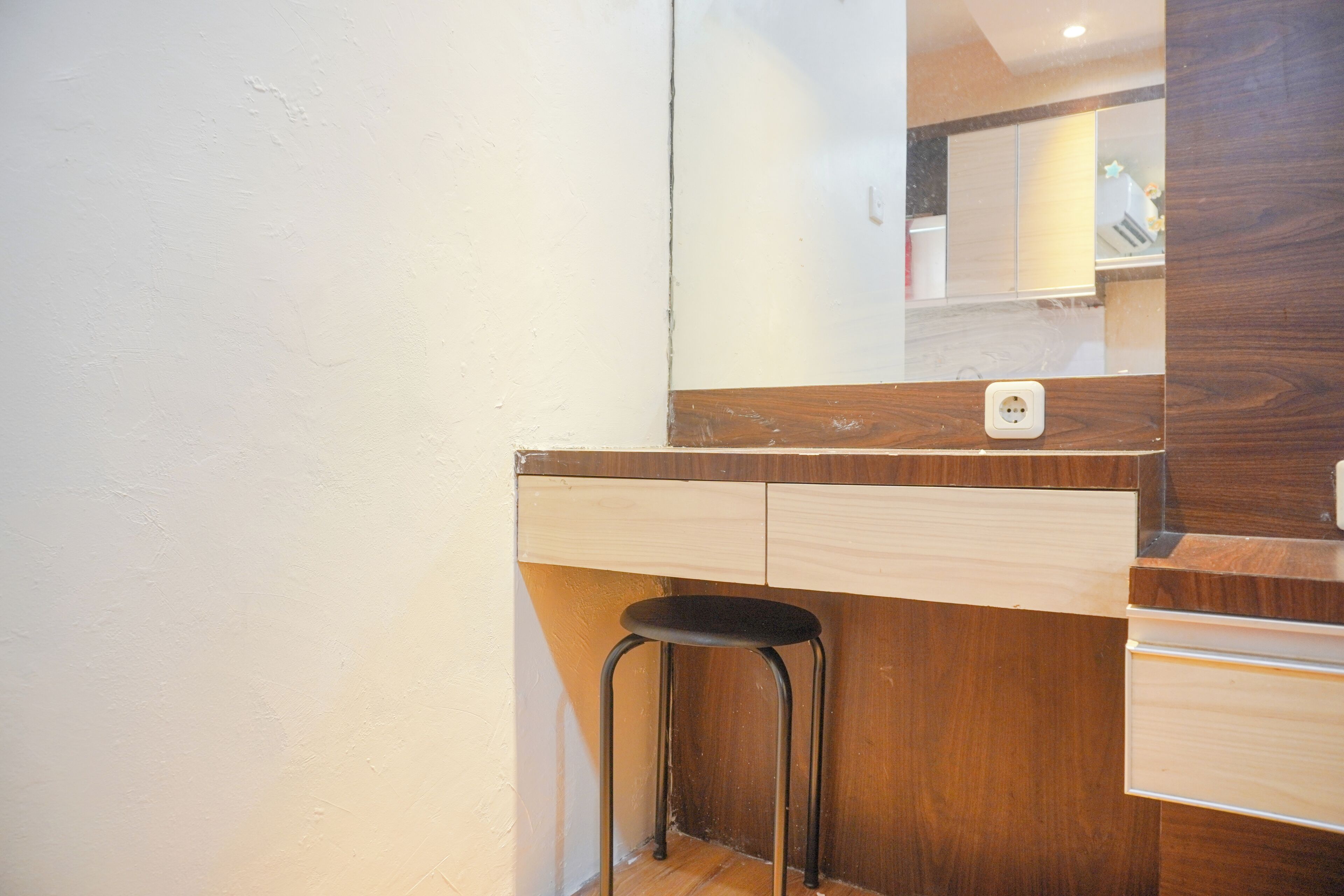 Una pequeña kitchenette con cubierta de madera, un taburete negro y un espejo que refleja un baño.