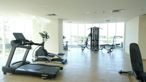 Une salle de sport équipée de machines de cardio, d’appareils de musculation et dotée de grandes fenêtres.