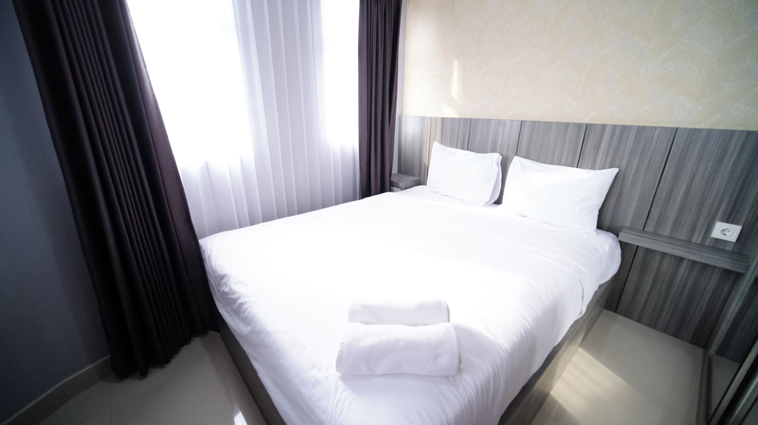 Ein Hotelzimmer mit einem ordentlich bezogenen Bett, einem Nachttisch und einer Lampe.