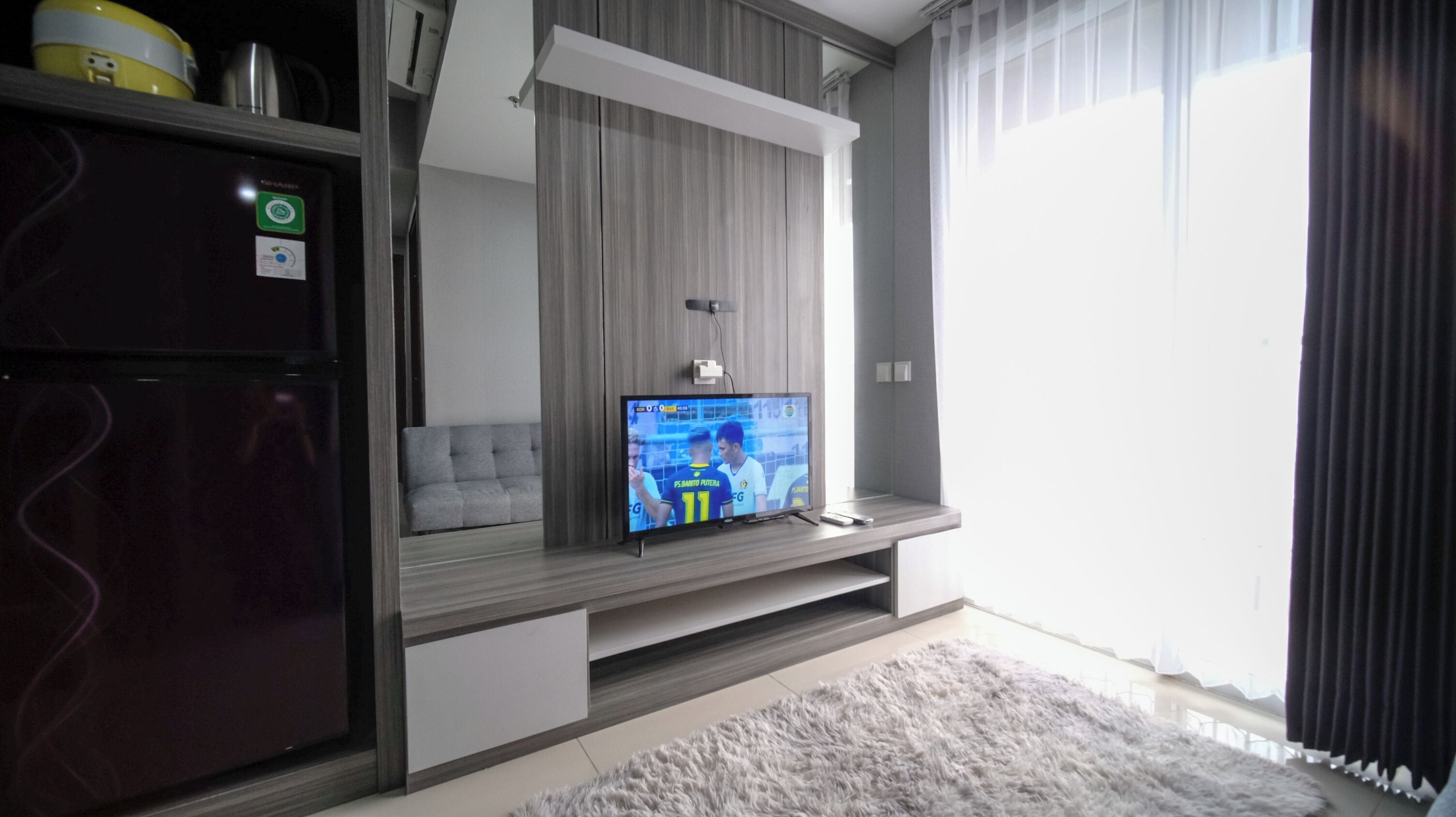 A modern living room with a flat-screen TV mounted on a wall, a grey sofa, a wooden cabinet, and a fluffy rug.