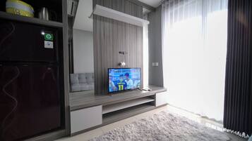 A modern living room with a flat-screen TV mounted on a wall, a grey sofa, a wooden cabinet, and a fluffy rug.