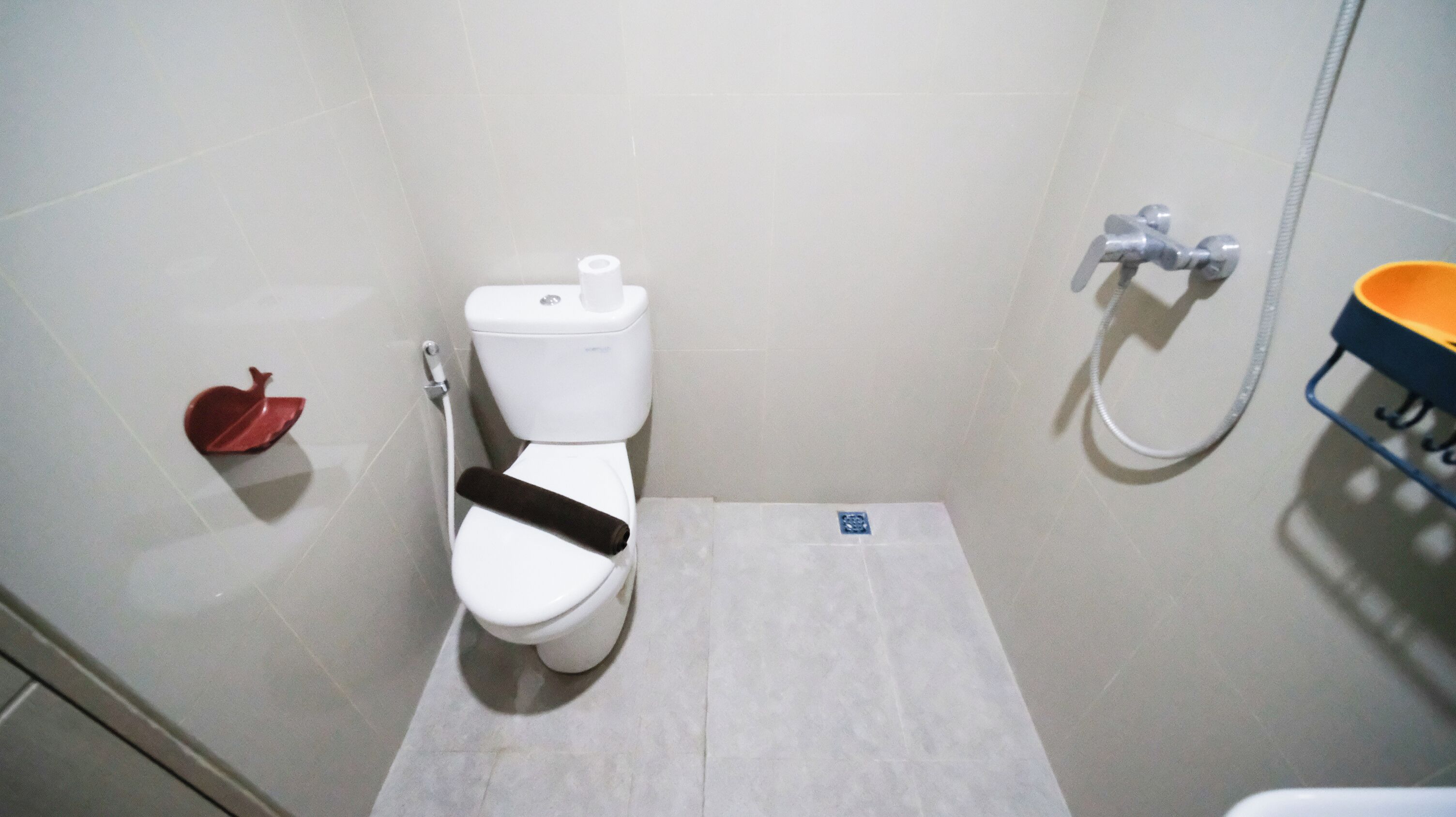 A small bathroom with a toilet, a shower, and a red object on the floor.