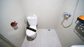 Et lille badeværelse med toilet, bruser og en rød genstand på gulvet.