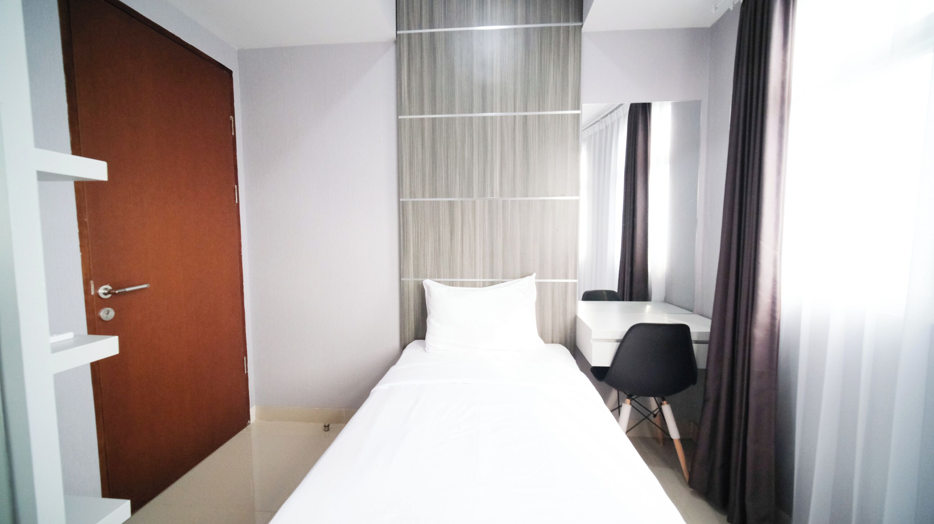 A hotel room with a bed, a desk, a chair, a door, and a curtain.