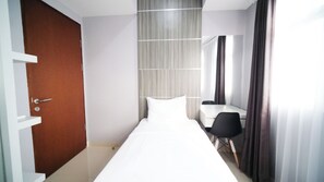 A hotel room with a bed, a desk, a chair, a door, and a curtain. - Good Choice And Spacious 2Br At Grand Dharmahusada Lagoon Apartment (Surabaya)