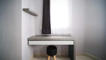 A room with a grey wall, a white desk with a black stool, and a window with sheer curtains.
