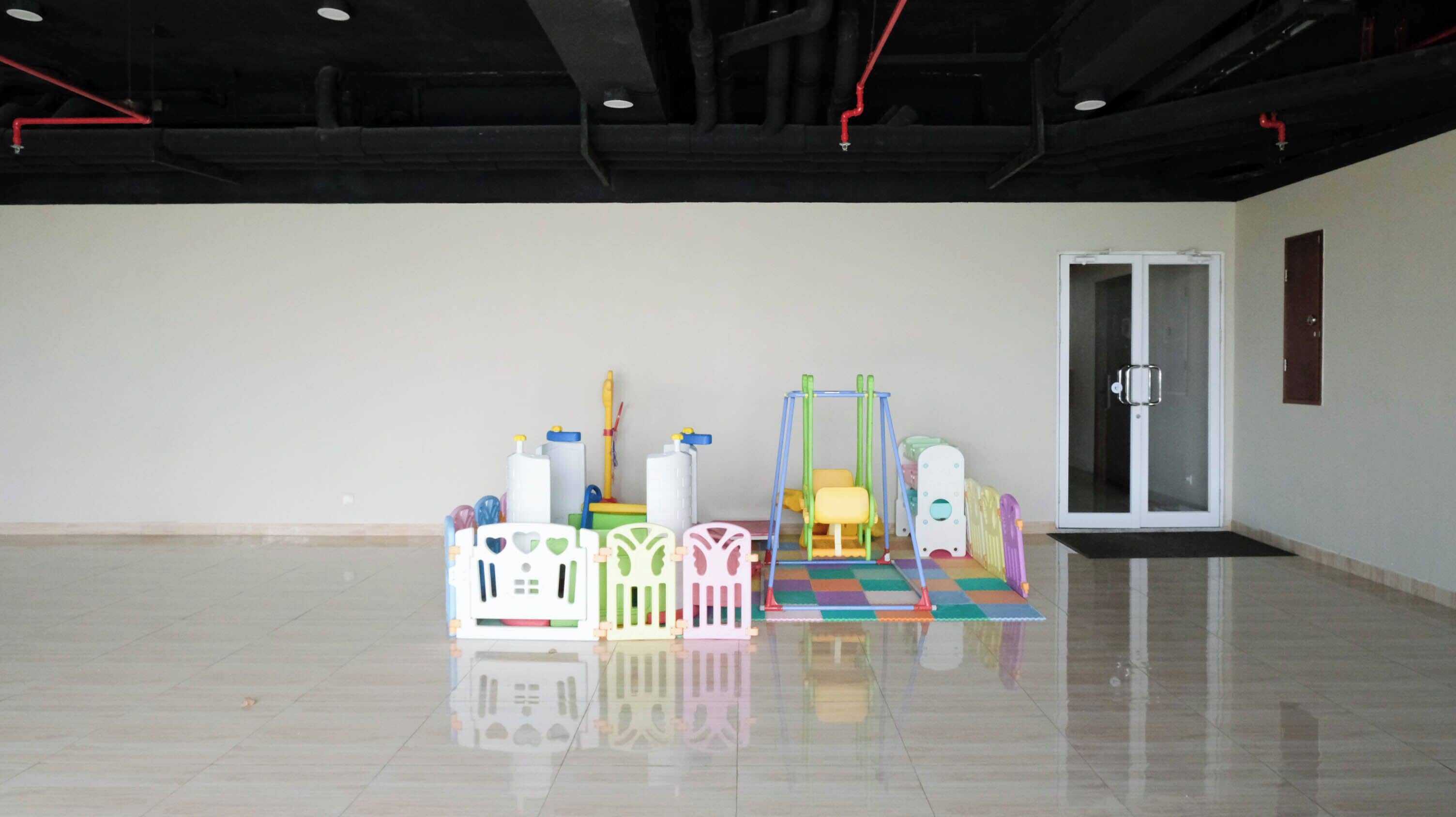 A spacious, empty room with a polished floor, a door, and colorful play equipment.