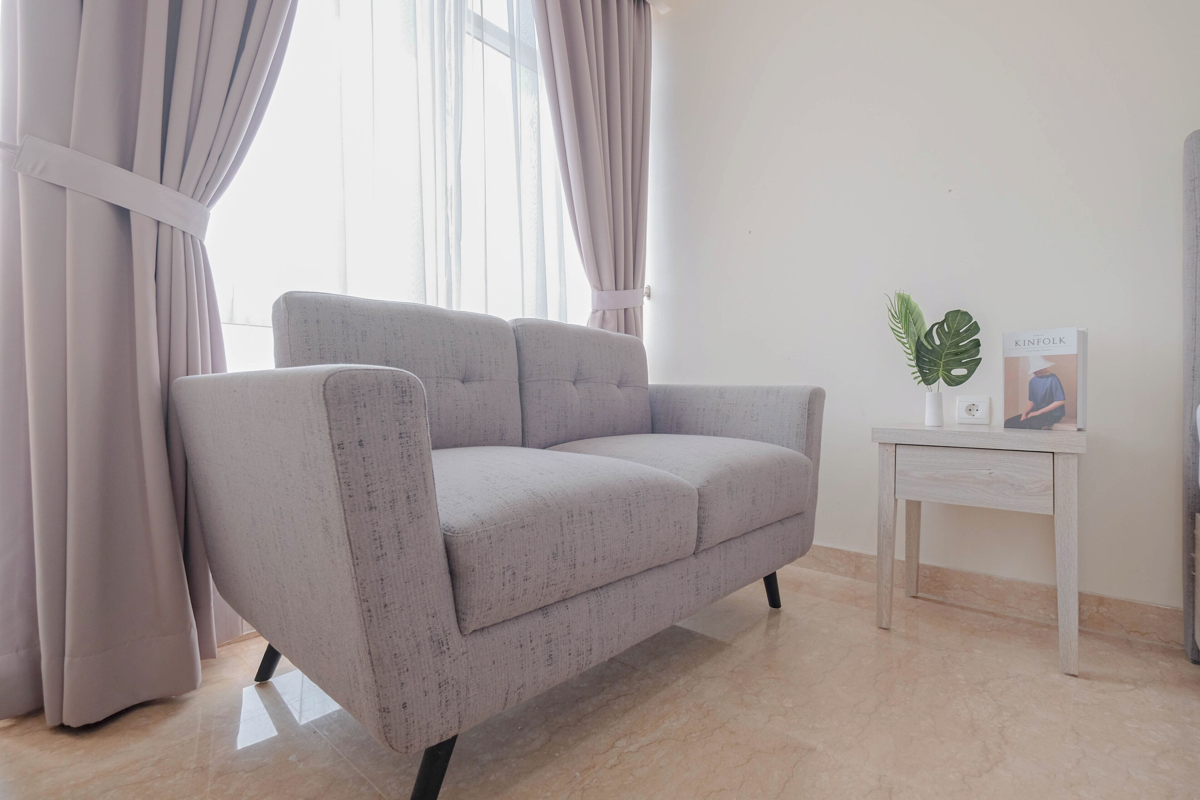 Una sala de estar moderna con un sofá gris, una mesita auxiliar y una ventana con cortinas.