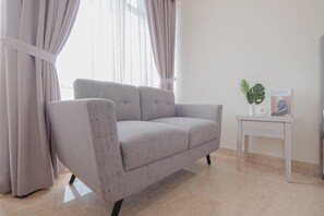 A modern living room with a grey sofa, a small side table, and a window with curtains. - Best Location And Comfy Studio At Menteng Park Apartment (Jakarta)