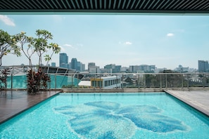 Ein Pool auf dem Dach mit Blick auf die Stadtlandschaft, umgeben von Glasgeländern und Topfpflanzen.
