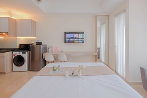 Ein Hotelzimmer mit einem Bett, einem Schreibtisch, einer Waschmaschine, einem Kühlschrank und einem an der Wand montierten Fernseher.