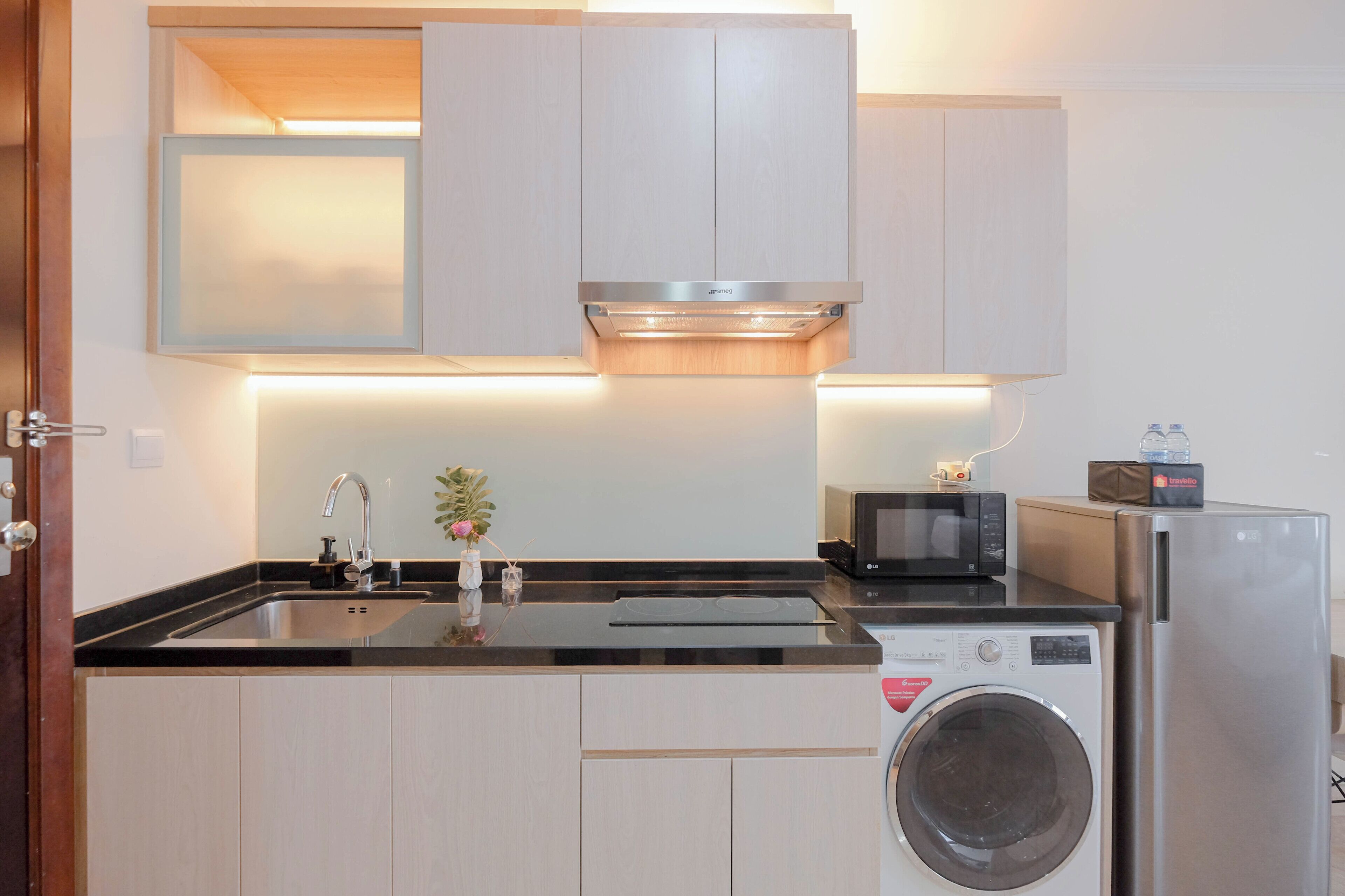 Una cocina compacta con lavadora integrada, microondas y un lavamanos con grifo.