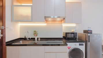 Una cocina compacta con lavadora integrada, microondas y un lavamanos con grifo.
