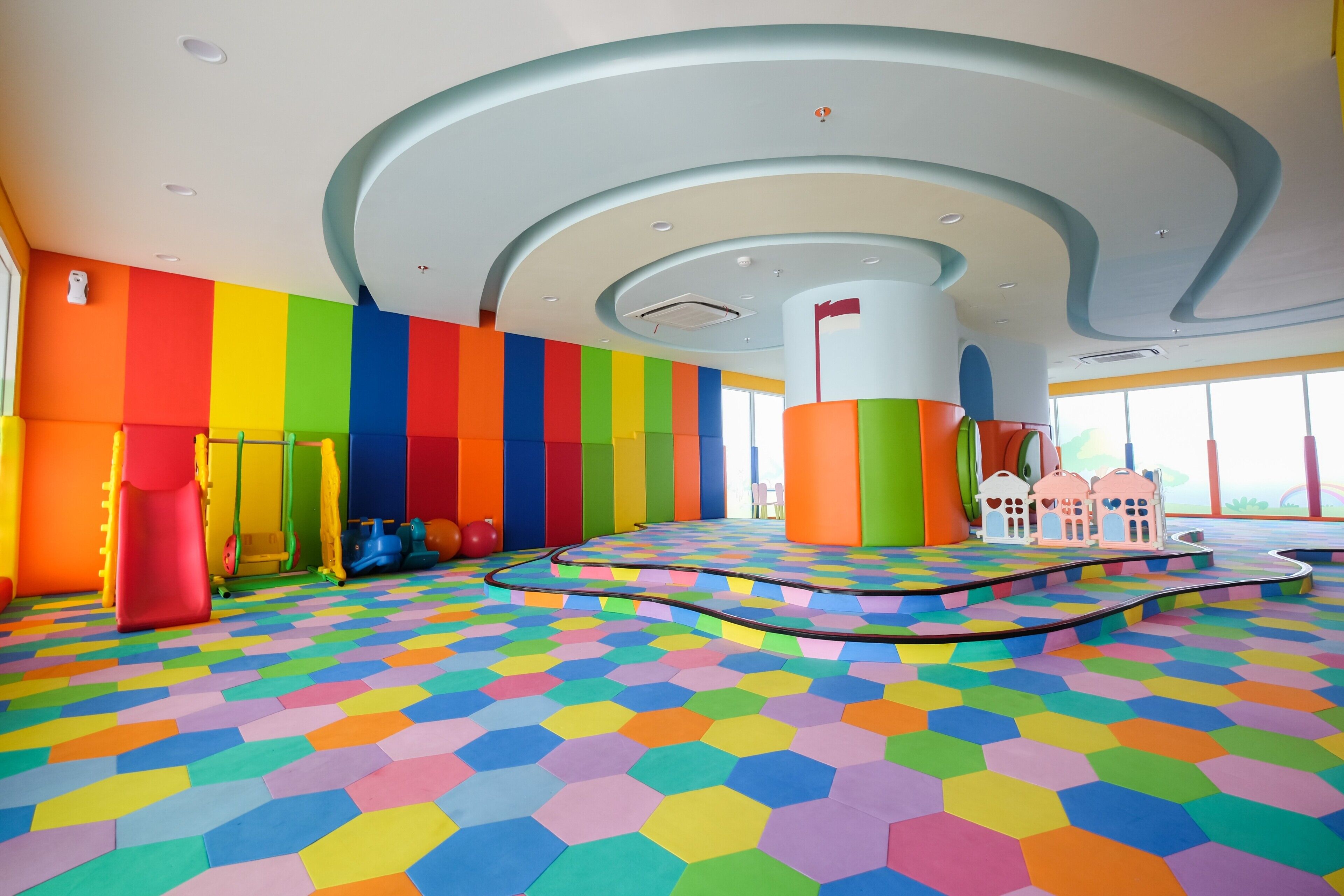 Un área de juegos colorida con piso y paredes multicolores, un pilar central y una estructura lúdica.