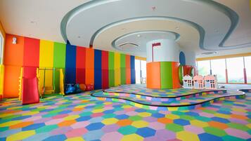 Un área de juegos colorida con piso y paredes multicolores, un pilar central y una estructura lúdica.