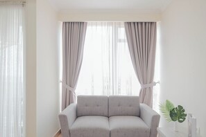 Una sala de estar con un sofá gris, cortinas de gasa y una planta en maceta.