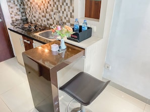 A kitchen with a sink, stove, and a countertop with a vase of flowers and water bottles. - Modern Look Studio At Grand Dhika City Apartment (Bekasi)