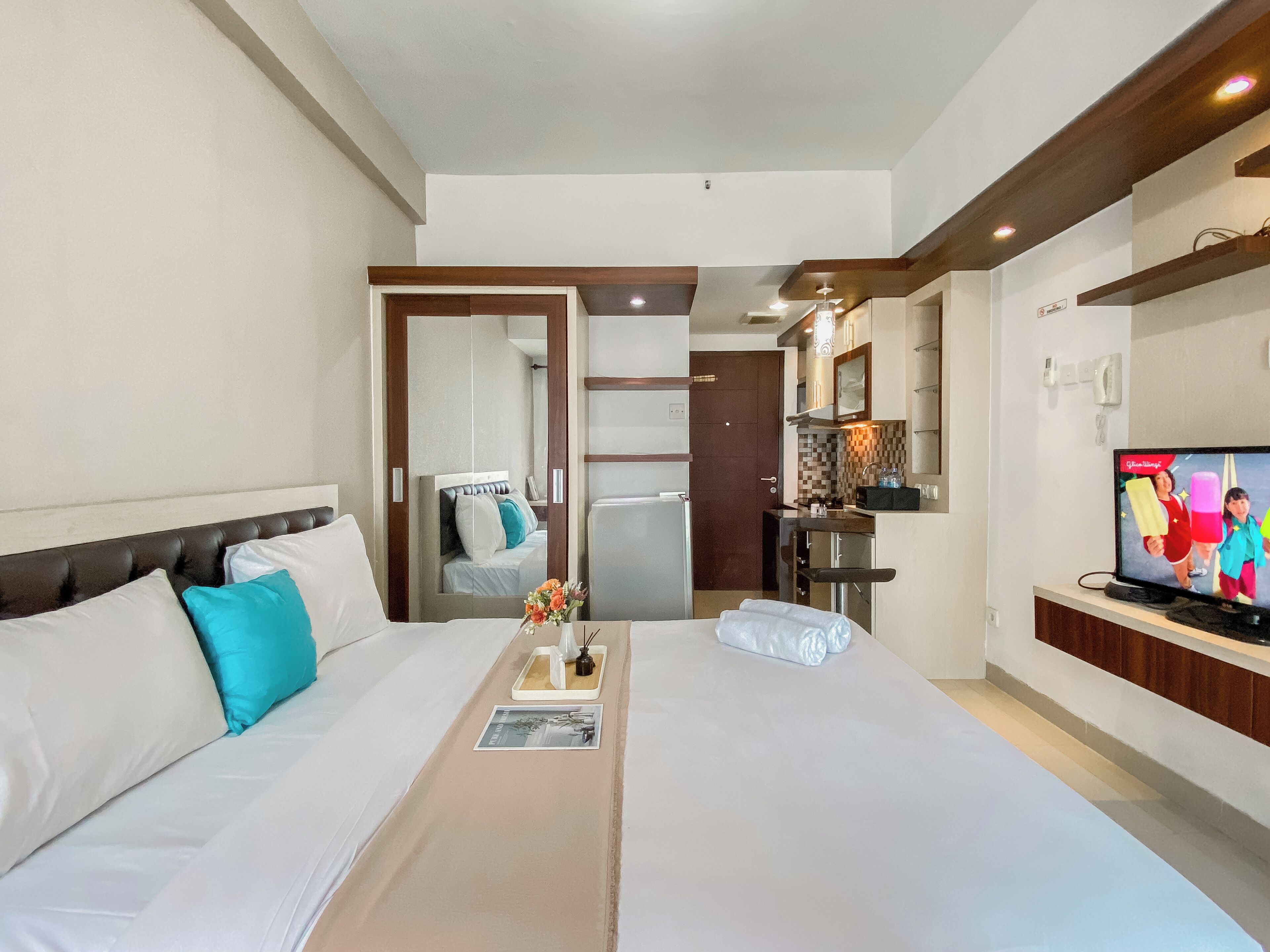 Habitación de hotel con cama, televisor, kitchenette pequeña y baño visible a través de una puerta.