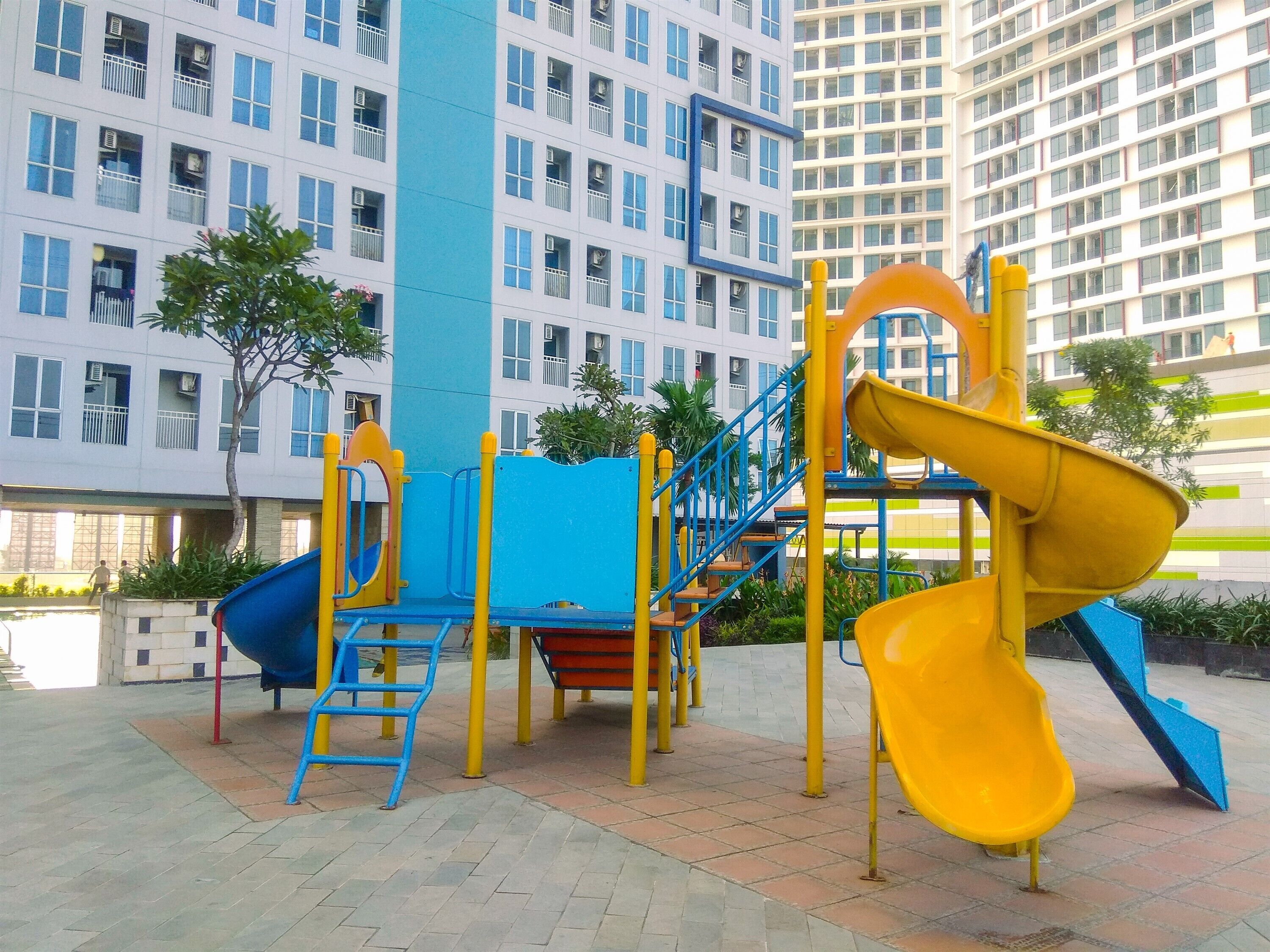 Un parque infantil con toboganes y estructuras para escalar, rodeado por un edificio con varias ventanas y balcones.