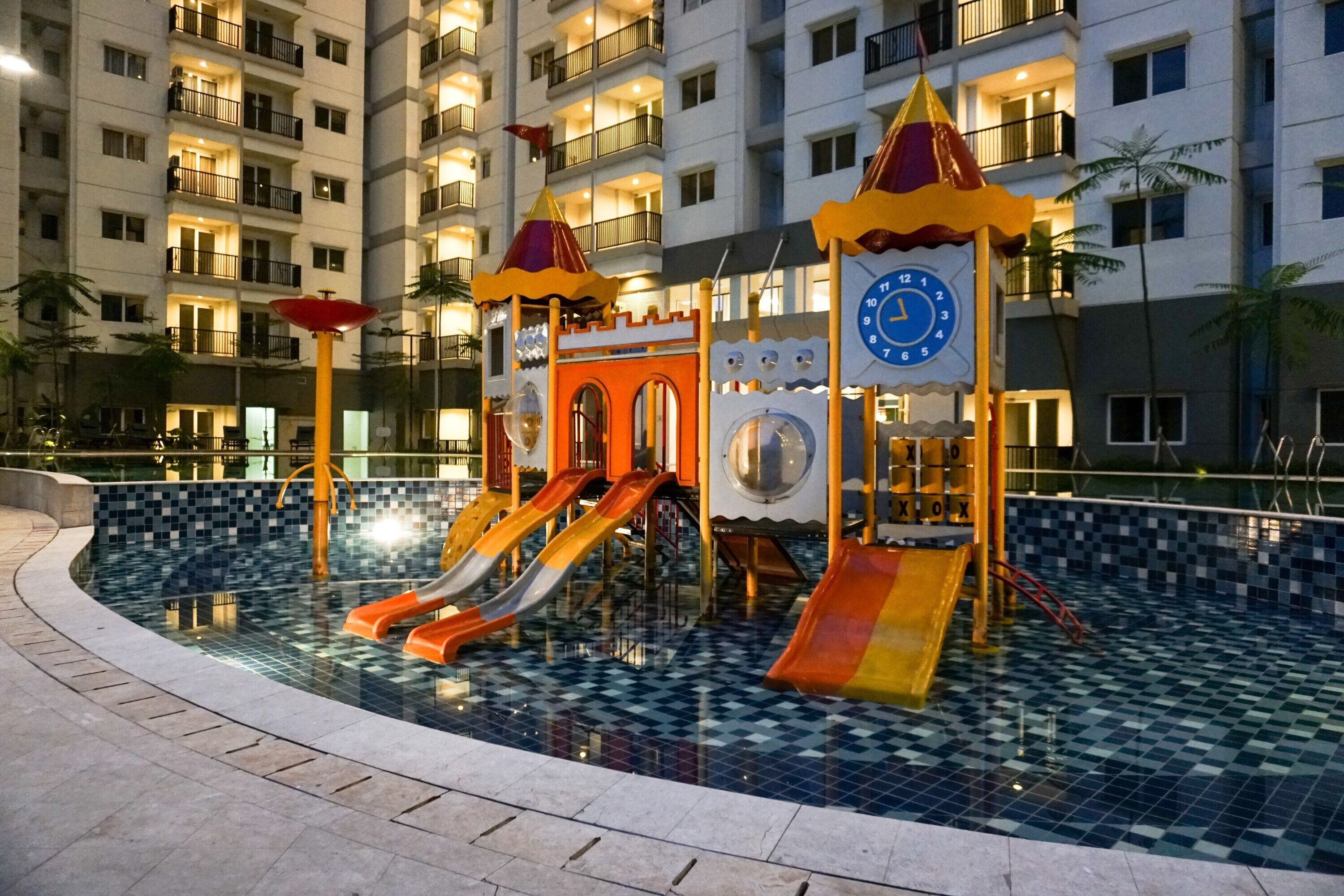 A children's play area with slides and a clock tower, surrounded by a pool with a checkered tile pattern.