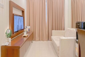 Une chambre d’hôtel avec une télévision, un bureau en bois, un canapé blanc et des rideaux beiges.