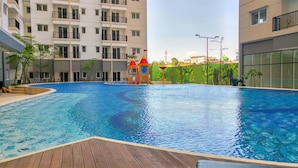 A swimming pool with a wooden deck, surrounded by multi-story buildings with balconies. - Minimalist And Good Place 1Br At Signature Park Grande Apartment (Jakarta)