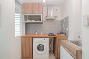 A compact kitchen with wooden cabinets, a built-in washing machine, a gas stove, and a modern backsplash. - 2Br Apartment Near Pakuwon Mall Bekasi At Grand Kamala Lagoon (Bekasi)