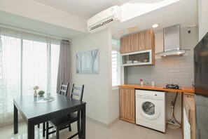 Et moderne køkken med en indbygget vaskemaskine, et spiseområde med bord og stole, samt et vindue med gardiner.