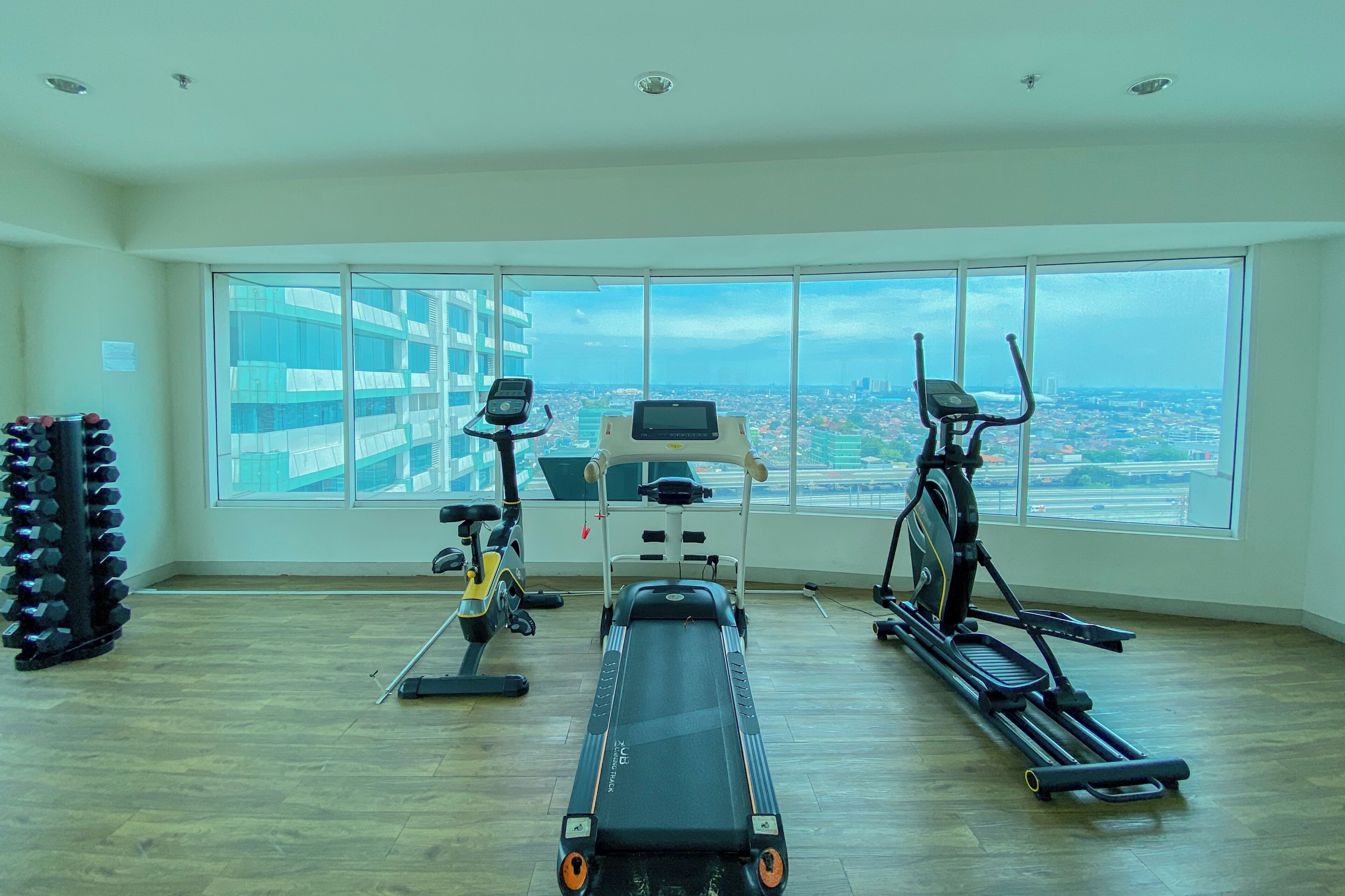 A spacious gym with a rowing machine, elliptical, and treadmill, large windows with a city view.