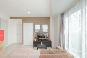 A modern living room with a sofa, a television, and a window with curtains. - 2Br Apartment Near Pakuwon Mall Bekasi At Grand Kamala Lagoon (Bekasi)