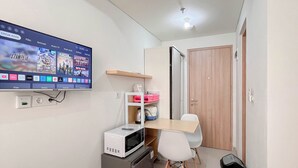 A small kitchenette with a microwave, a mini fridge, and a TV mounted on the wall displaying a movie. - Restful Living Studio (No Kitchen) At Apartment Bandaraya - Tallasa City Makassar (Makassar)