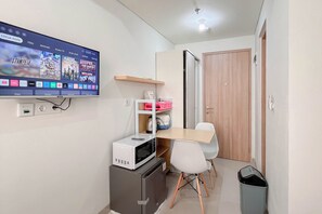 A small kitchenette with a microwave, a mini fridge, and a TV mounted on the wall displaying a movie. - Restful Living Studio (No Kitchen) At Apartment Bandaraya - Tallasa City Makassar (Makassar)