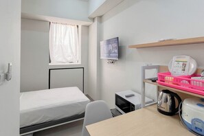 A compact hotel room with a single bed, a desk with a computer, a kettle, and a microwave. - Restful Living Studio (No Kitchen) At Apartment Bandaraya - Tallasa City Makassar (Makassar)