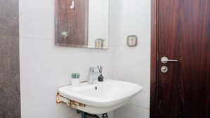 Un bagno con un lavandino bianco, uno specchio, una porta in legno e una piccola pianta in vaso.