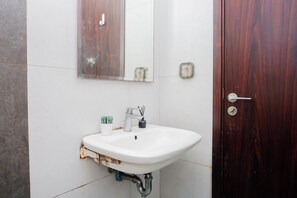 Ein Badezimmer mit einem weißen Waschbecken, einem Spiegel, einer Holztür und einem kleinen Topfpflanzen.