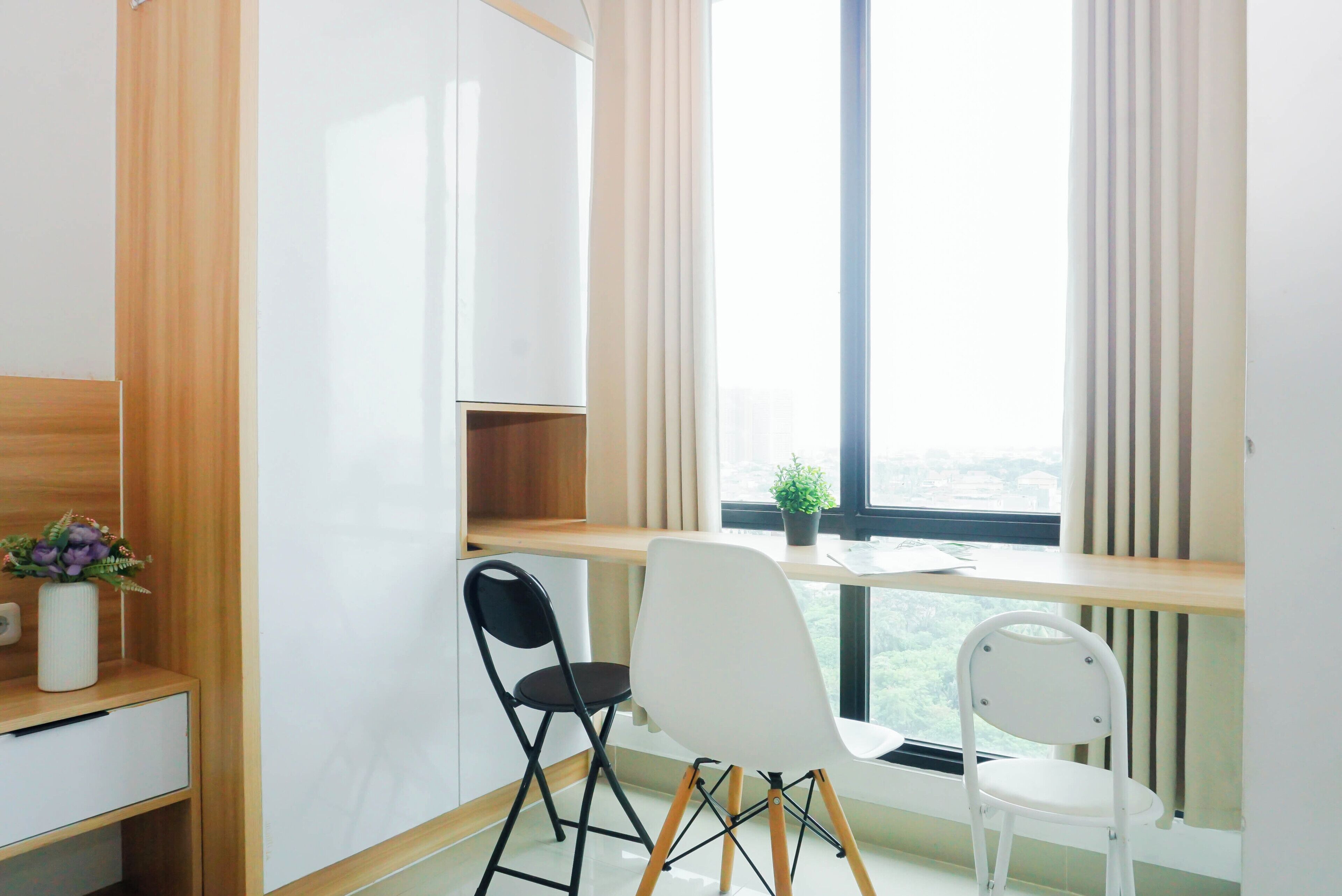 Ein Zimmer mit Schreibtisch, zwei Stühlen, einer Topfpflanze und einem Fenster mit Blick.
