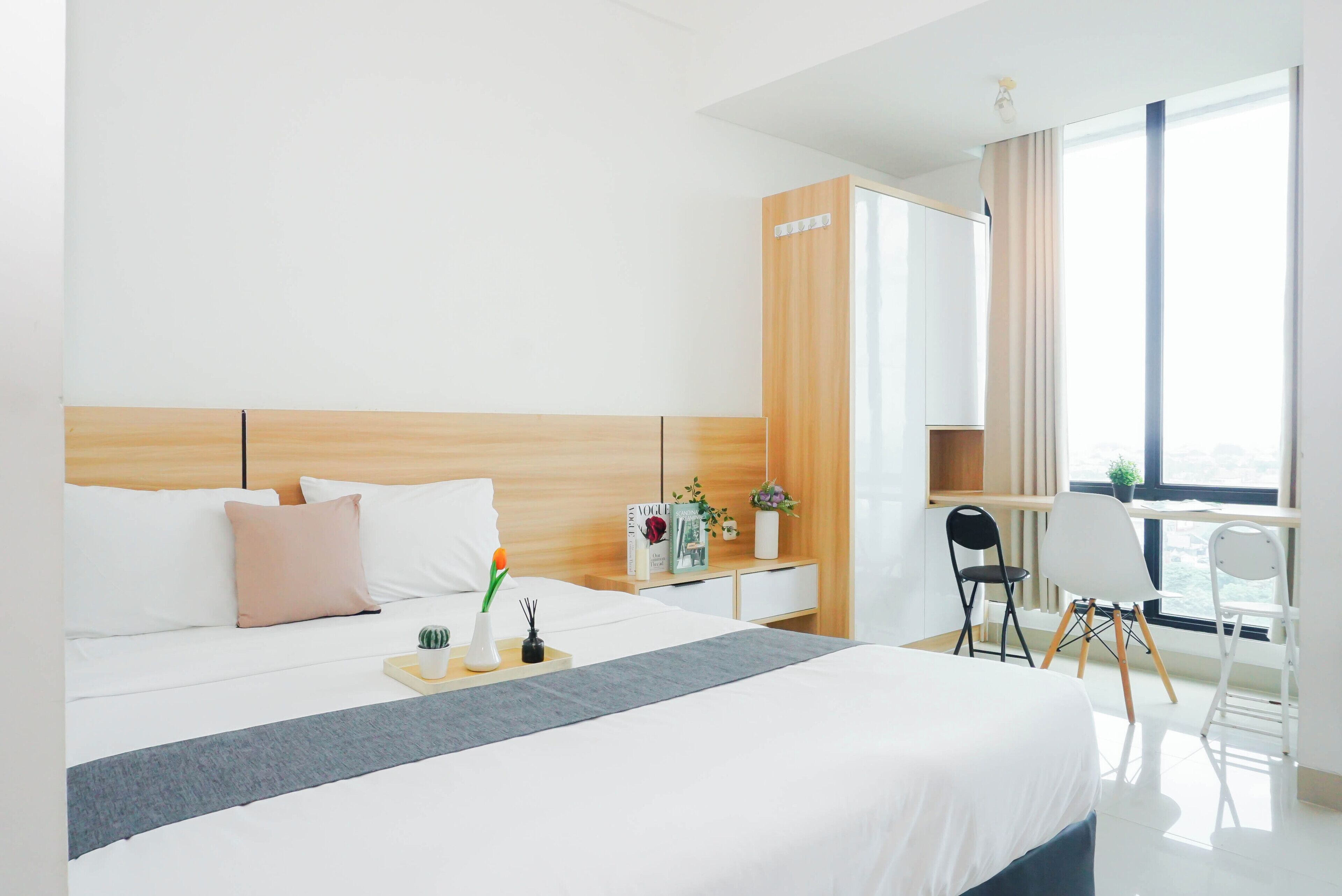 Ein Hotelzimmer mit Bett, Nachttisch, Schreibtisch mit Stuhl, Fenster mit Vorhängen und einem Kleiderschrank.